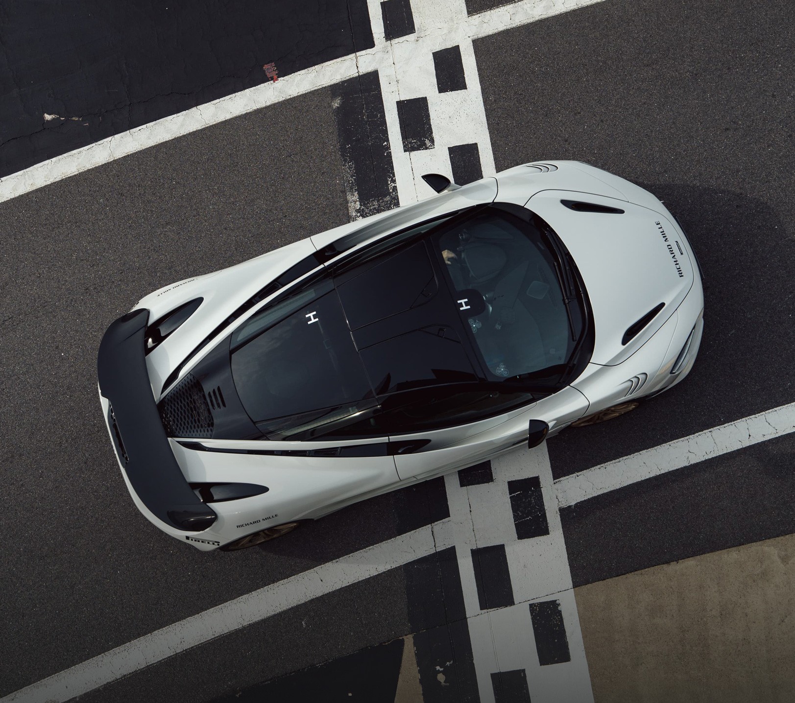White McLaren Artura high-performance hybrid supercar driving at speed on the Silverstone Grand Prix circuit in the UK, indicated by the track barriers and pit-lane exit area.
