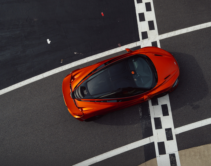 An overhead shot of a burnt orange McLaren supercar stationary on a race track.
