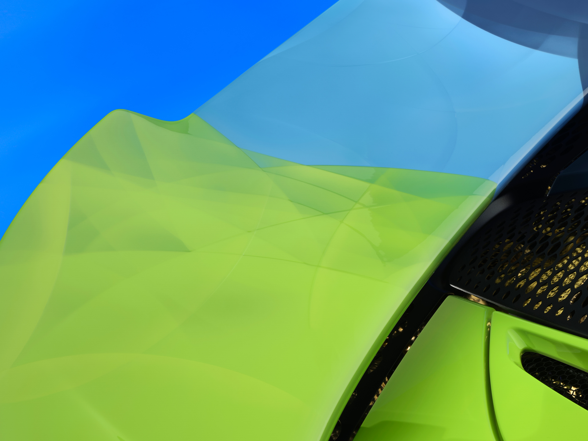 The rear wing of the Project Chromology 750s by MSO and Nat Bowen, on display against a glowing blue background. The car is various overlaying shades of green and blue and can be seen parked at an angle with its headlights on.