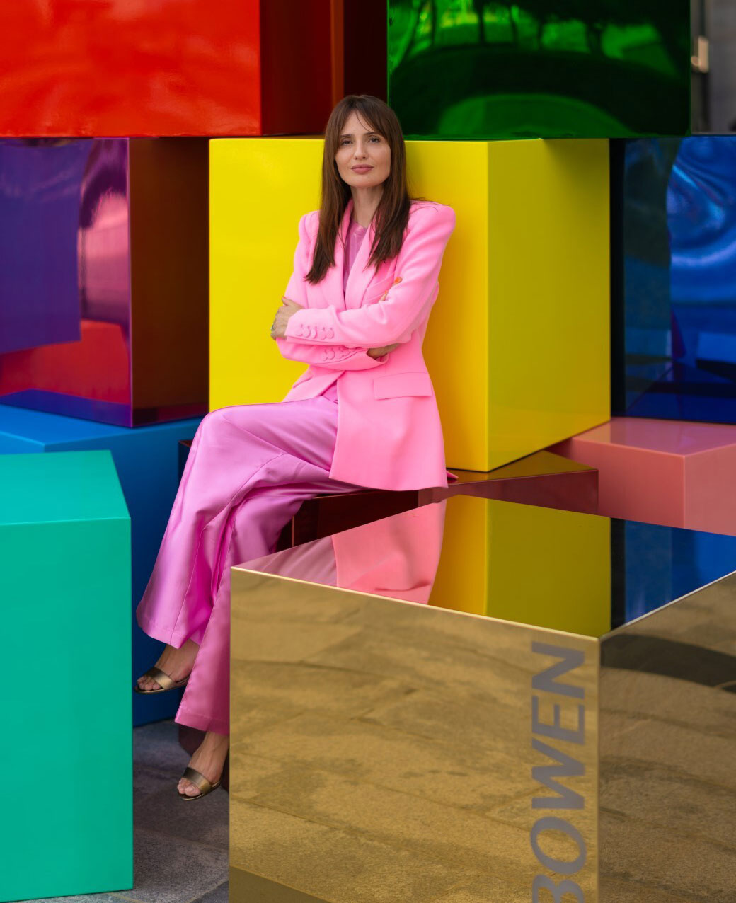 Artist Nat Bowen posing with her arms crossed wearing an all pink outfit, stood in front of a metallic multicoloured McLaren car.i