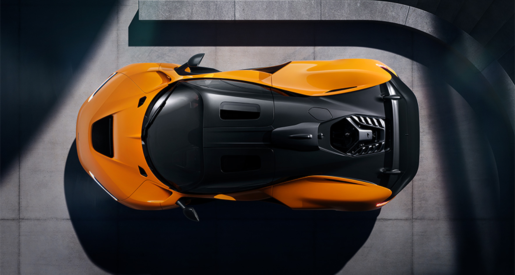 A high aerial shot of an orange McLaren W1, with a concrete perimeter showing the car from above.