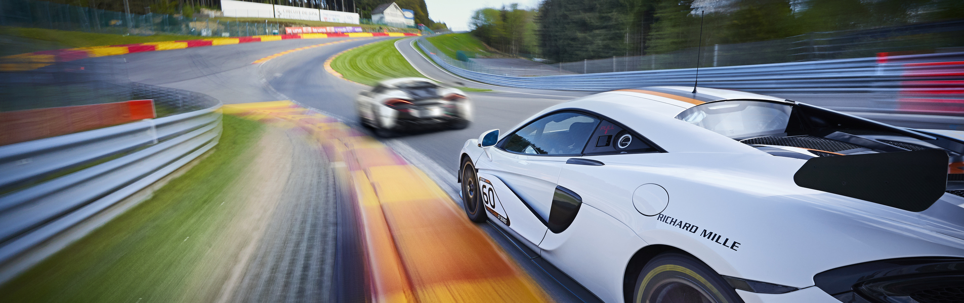 Blurry image of McLaren cars racing on a track at speed.