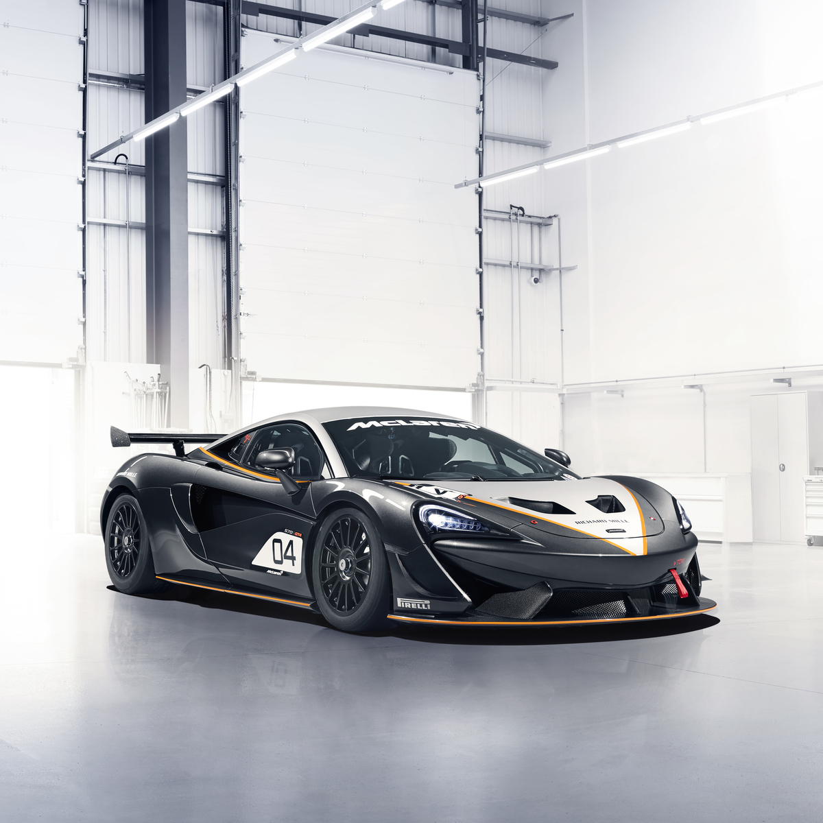 Black, white and orange McLaren 570S GT4 parked in a bright warehouse. 