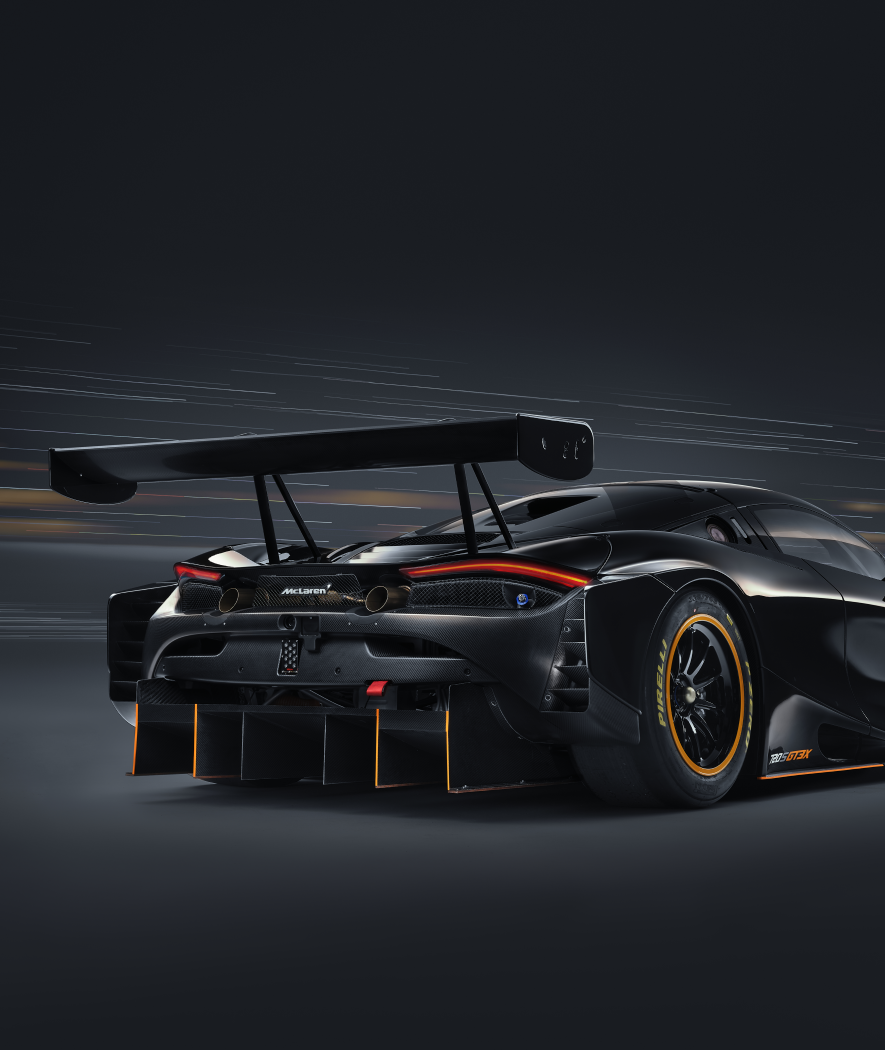 Rear view of back McLaren 720S GT3 X with orange detailing on a dark, blurry background.