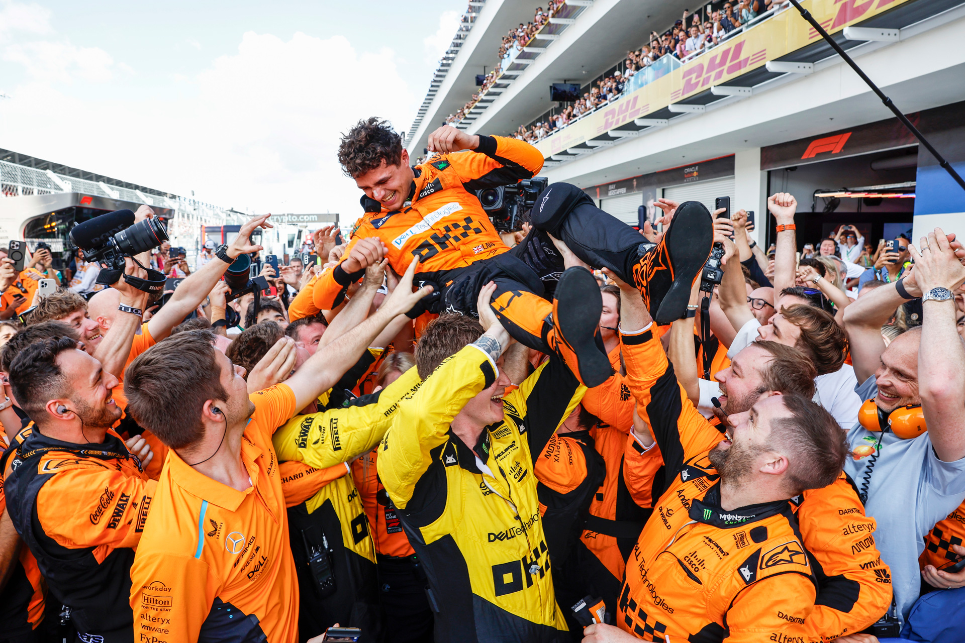 Lando Norris being lifted jubilantly by the cheering McLaren crew after a victory.