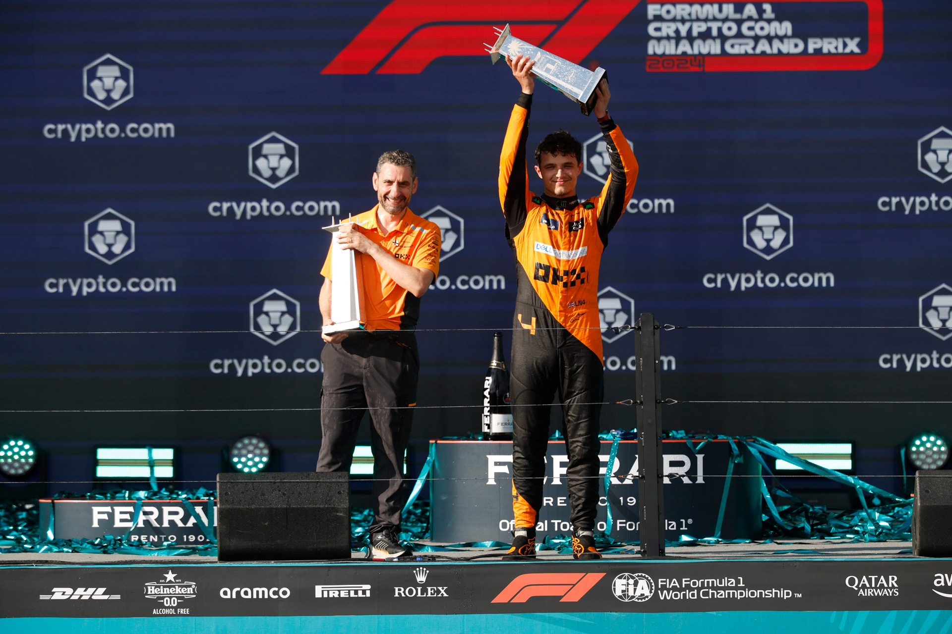 Lando Norris and Andrea Stella celebrating on the podium with trophies. 