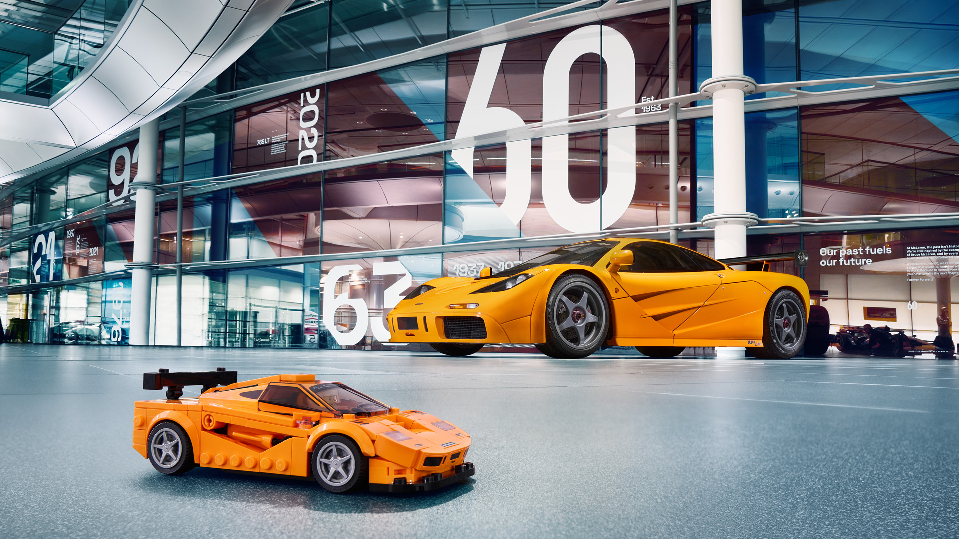 Orange McLaren F1 parked behind its Lego replica in the McLaren Technology Centre.