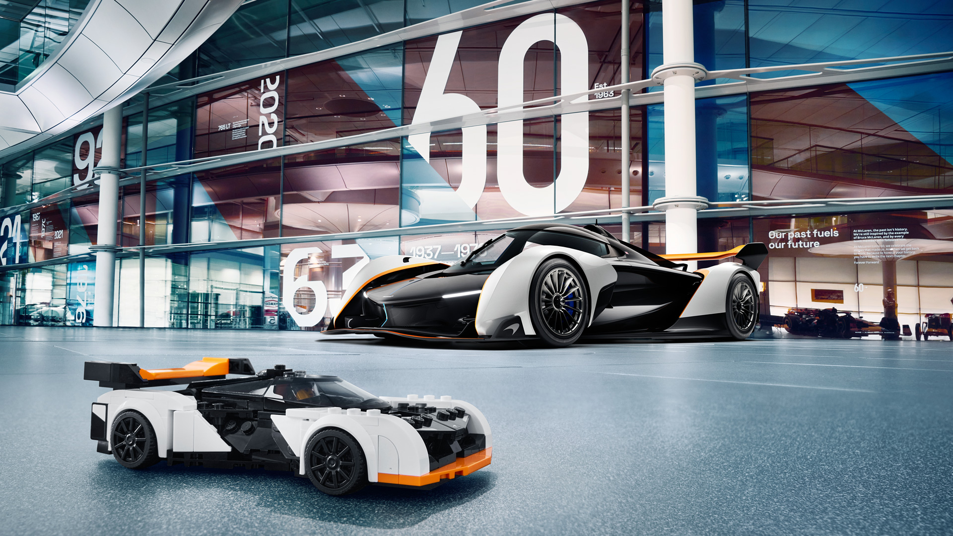 Black, white and orange McLaren Solus GT parked behind its Lego replica in the McLaren Technology Centre.