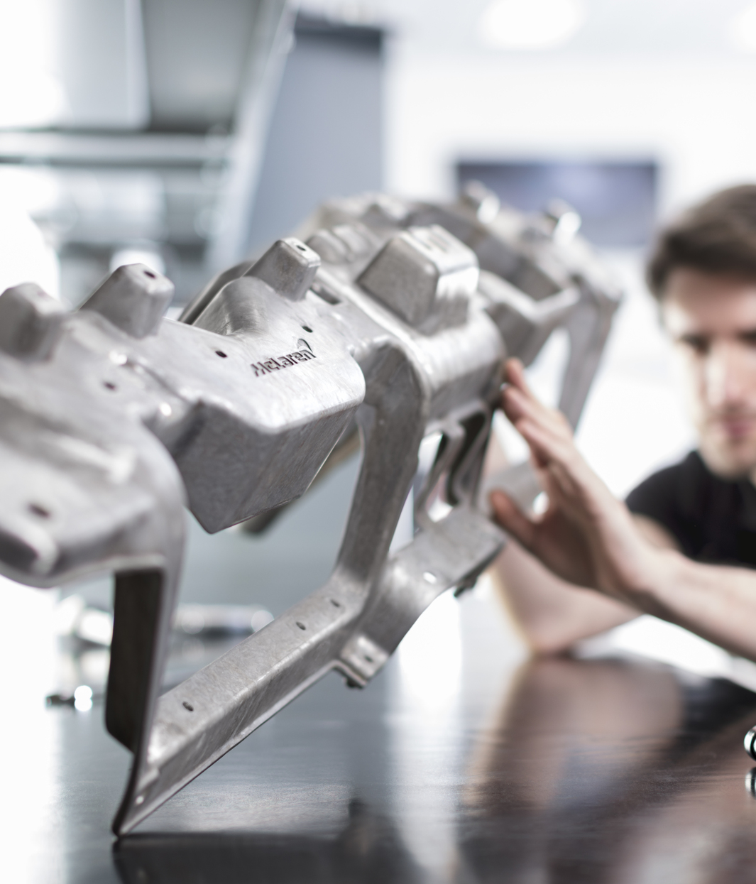 A male McLaren engineer inspecting a car component in a workshop.