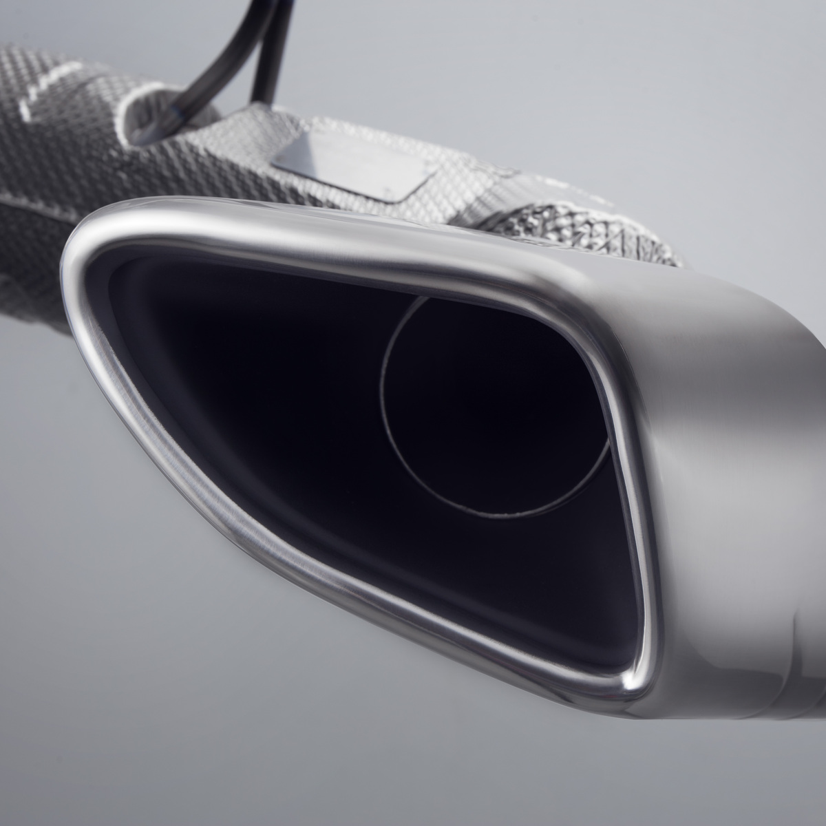 A close-up of a McLaren's polished chrome exhaust pipe, highlighting the car's intricate details.