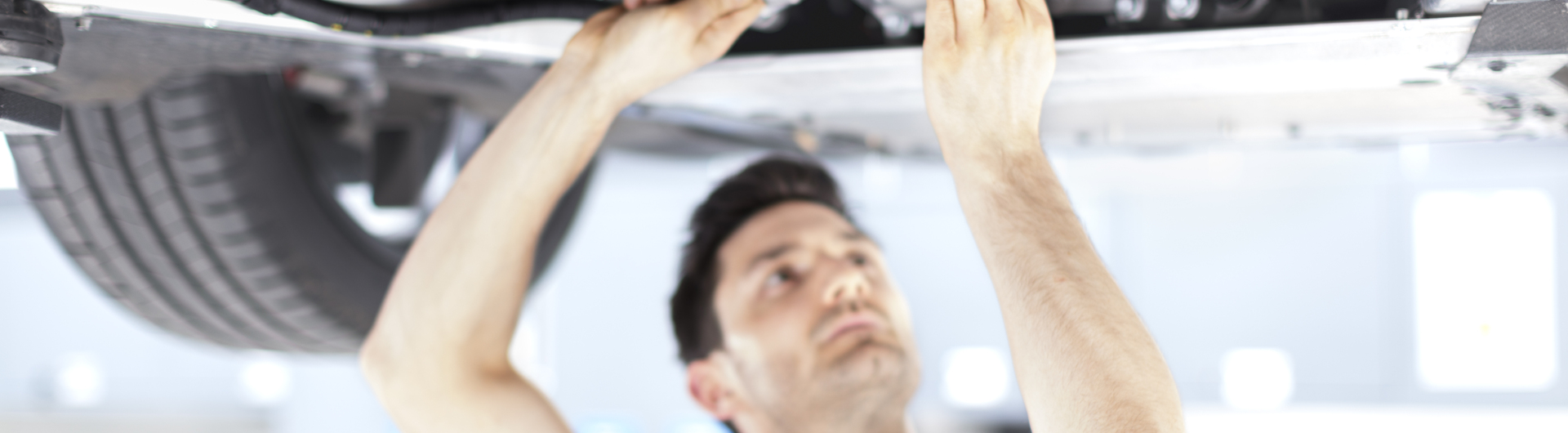 A McLaren mechanic in a black polo shirt, working on the underside of a car.