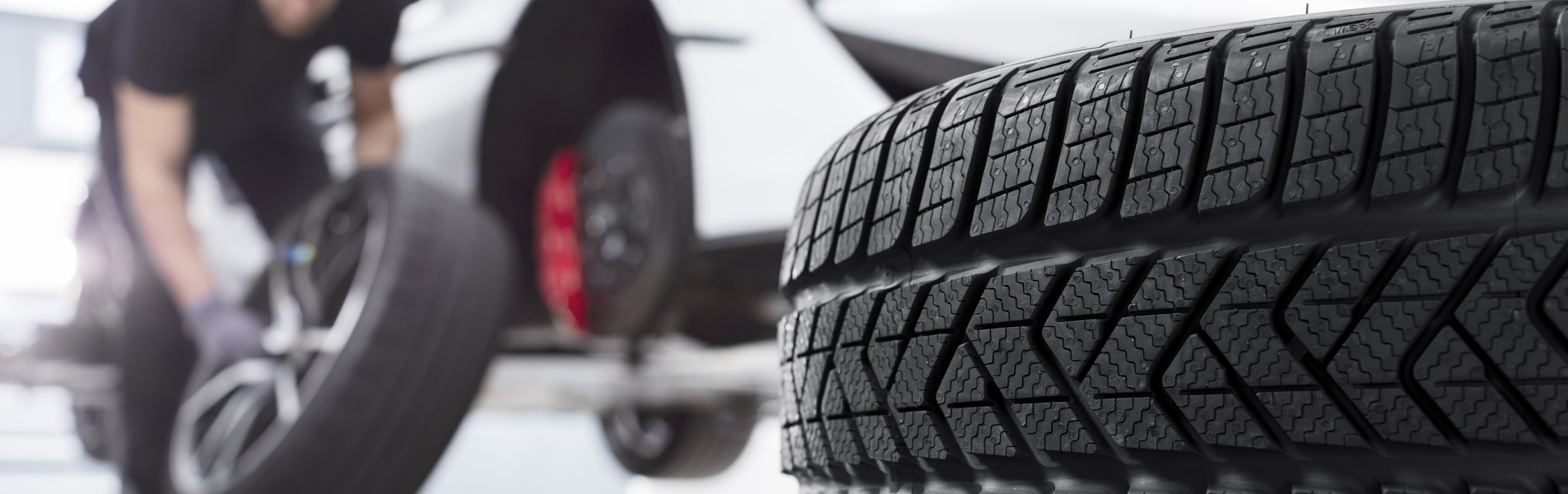 A large tire in the foreground with a McLaren technician changing a wheel on a white supercar in the background.