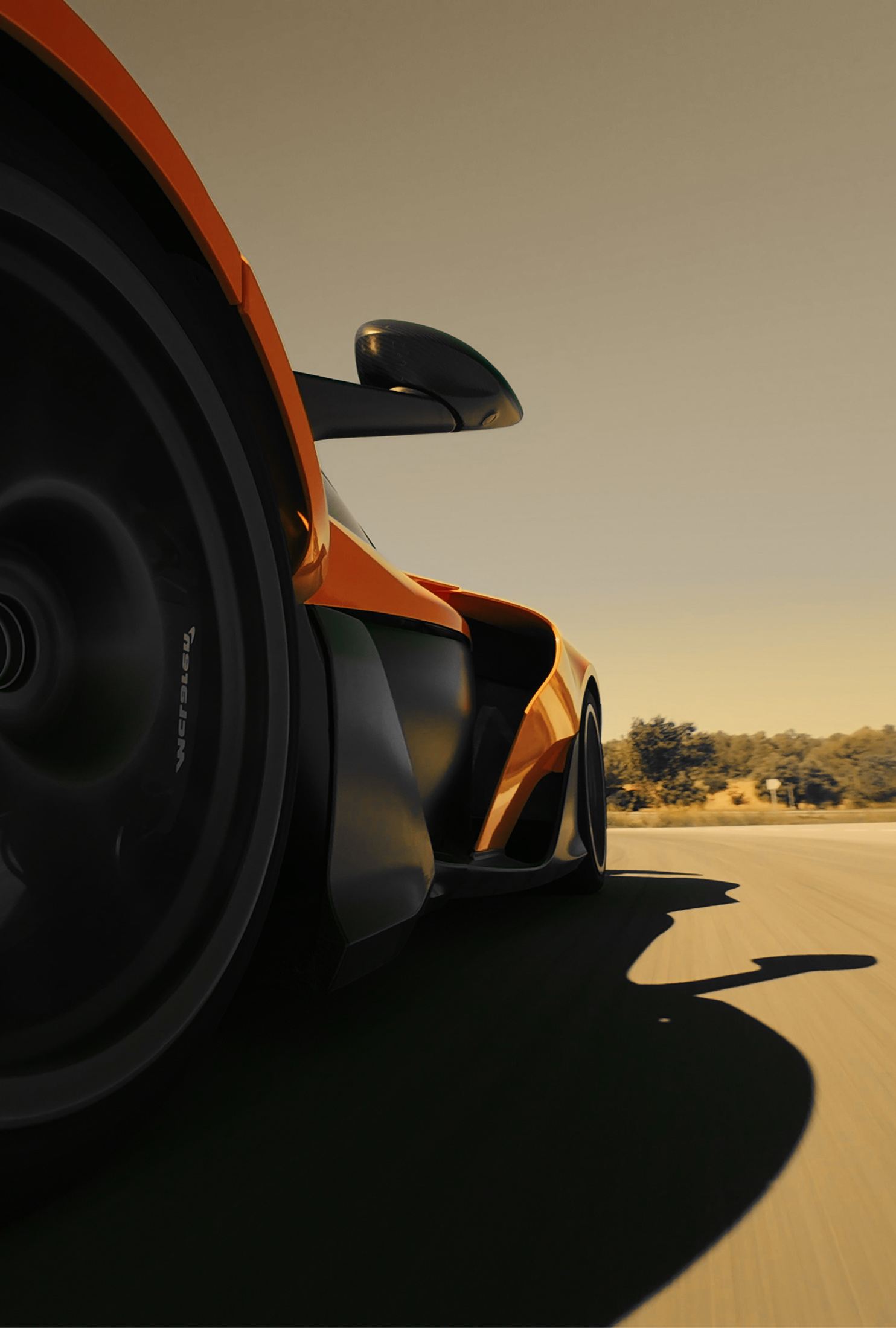 A low-angle, side view of an orange and black McLaren supercar with a large wheel in the foreground, speeding along a sunlit road, casting a long shadow.