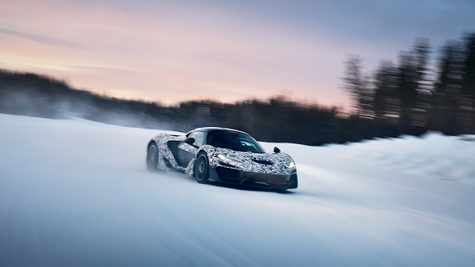 A camouflage-wrapped McLaren W1 prototype drifts on a snowy surface at dusk or dawn, with a blurred forest in the background.